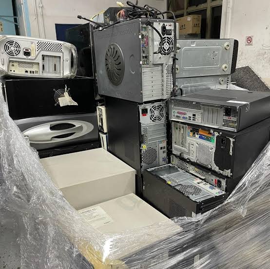 A large stack of old desktop computers, servers, and electronic equipment wrapped in clear plastic, possibly prepared for recycling or disposal in an indoor industrial setting—ideal for those looking to Sell Scrap & 回收 (recycle).