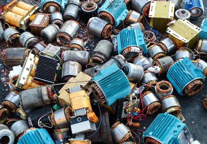 A pile of discarded electric motors and various metal components, including blue and yellow casings, copper wire coils, and circuit boards, lies on a dark surface—ready for Sell Scrap & 回收.